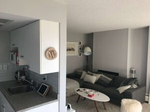 Photo of my lounge area with artwork about Manchester on the wall, dakrg rey sofa, white coffee table, and a circular wooden board with the WordPress logo on it. The walls are now finished with light grey, the ceiling is just off-white and there's a just-off white rug.